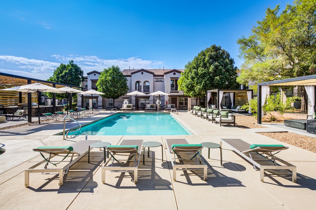 a swimming pool with chairs and umbrellas and a building in the background